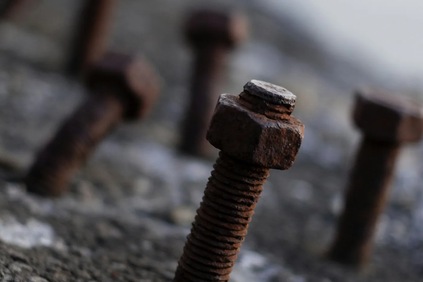 Rusted steel bolts standing proud of a corroded surface, threads and hex heads covered in red oxide